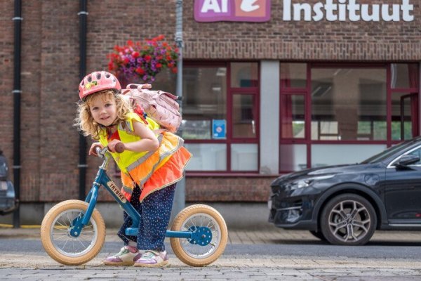 meisje op een loopfiets aan een schoolpoort